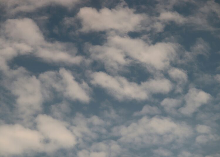 a plane flying through a cloudy blue sky